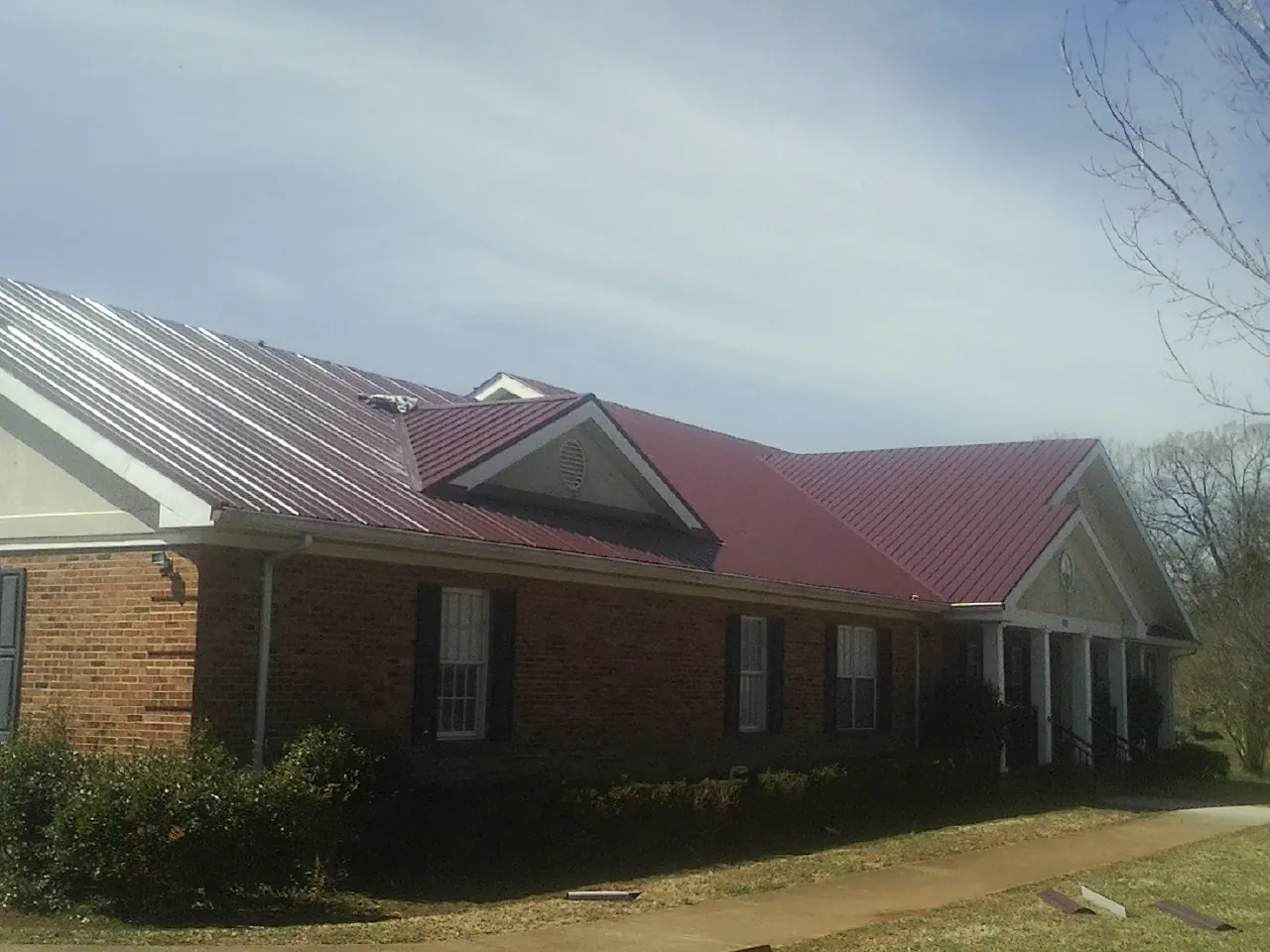 Red metal roof with gabled entries on a long brick building, from a Hail Damage Roof Repair job in Gambier