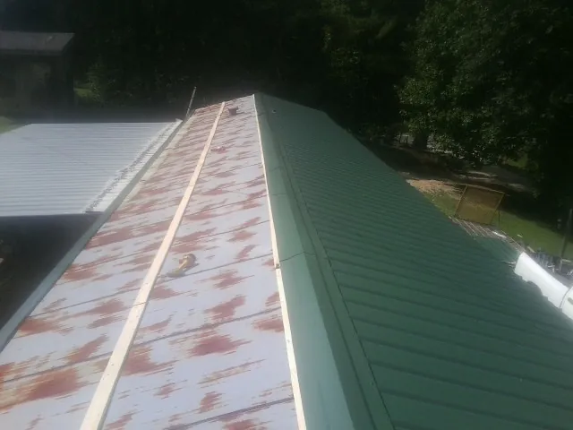 Old rusted panels beside newly installed green metal roofing — Wind Damage Roof Repair by Roofing Brothers in Gambier