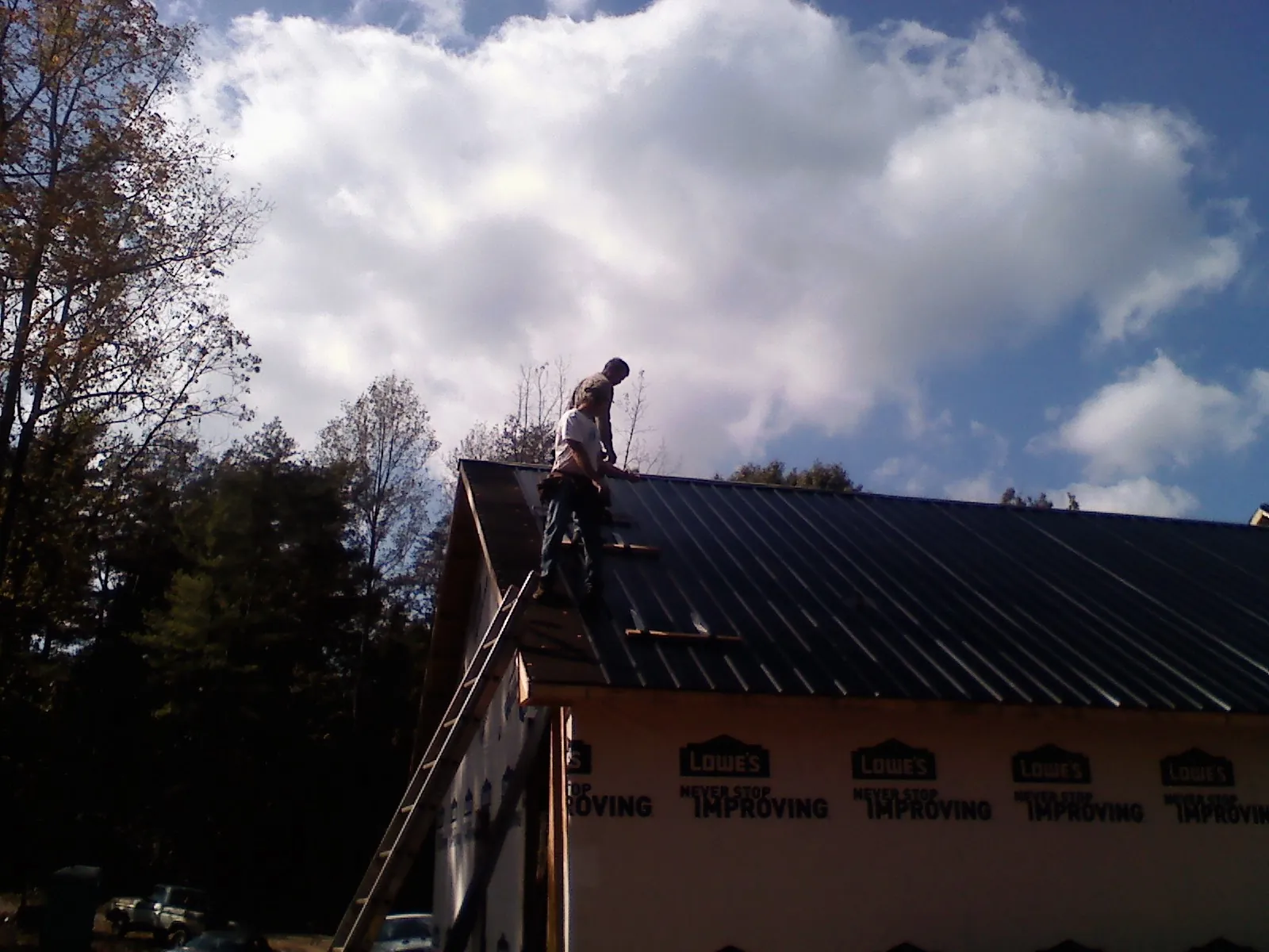 Roofer fastening dark metal panels high against a cloudy sky, from a Roof Inspection job in Gambier