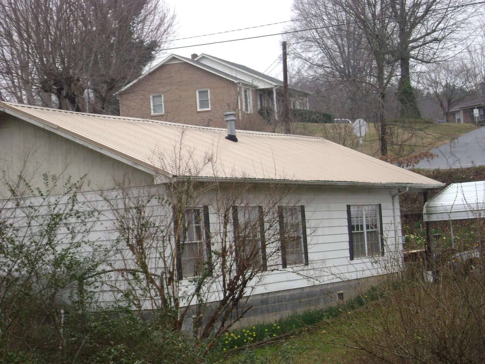 Tan metal roof on a white sided house set into a hillside — Commercial Roofing by Roofing Brothers in Gambier